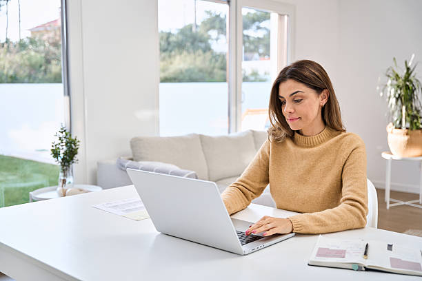 istock Smiling mature woman using laptop computer sitting at table in living room. 2238131483