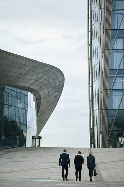 istock Three Middle Aged Caucasian Businesspeople Walking between Modern Office Buildings 2238131564