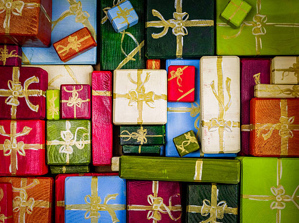 Top view of multiple handcrafted wooden blocks painted as festive gift boxes with gold ribbon patterns. The vibrant arrangement of red, green, blue, white, and orange presents creates a cheerful holiday atmosphere, perfect for Christmas themes, celebration decor, and creative design projects.