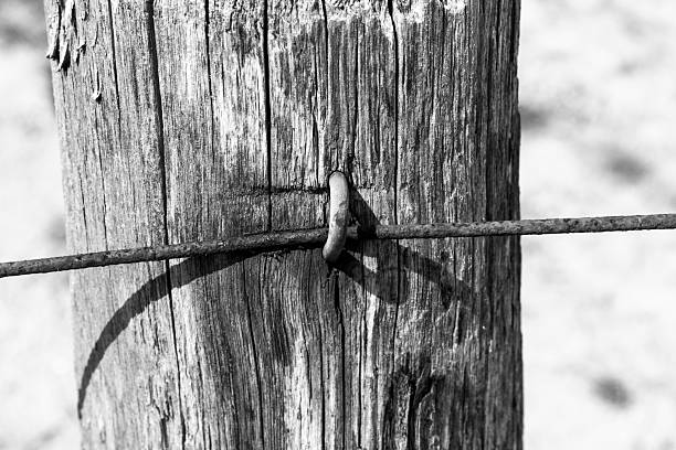 A close view of an old wooden fence post with a rusty metal wire looped around it. The focus is on the texture of the wood and the weathered metal in a quiet outdoor area.