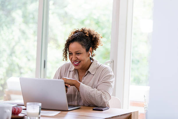 istock A cheerful woman smiles while working on her laptop at home with wireless earbuds. 2238138905
