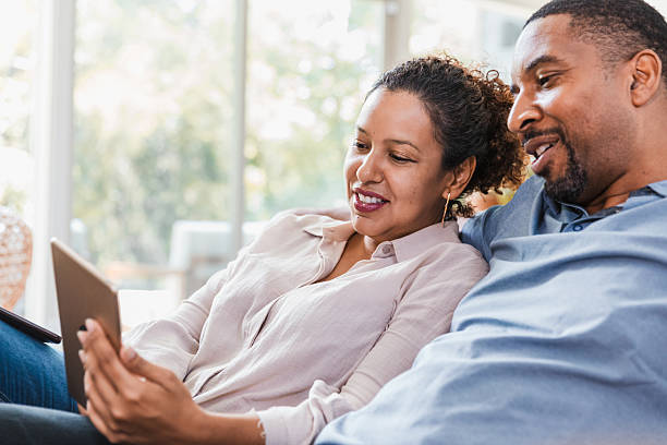 istock Couple using a digital tablet, looking and smiling at the screen together on a couch. 2238138936