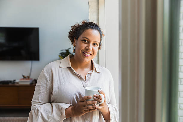 istock Smiling woman holds a mug of coffee while looking out a window 2238138940