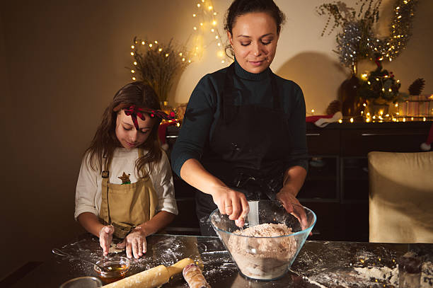 A mother and daughter bake together in a warm, festively lit kitchen. Flour, mixing bowl, and holiday decor create a joyful family scene as they prepare Christmas treats.