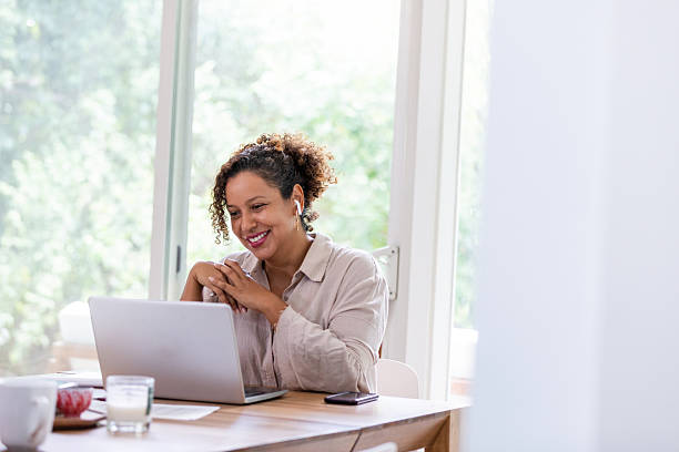 istock Smiling woman in casual clothing wearing earbuds while using a laptop at a table 2238143556