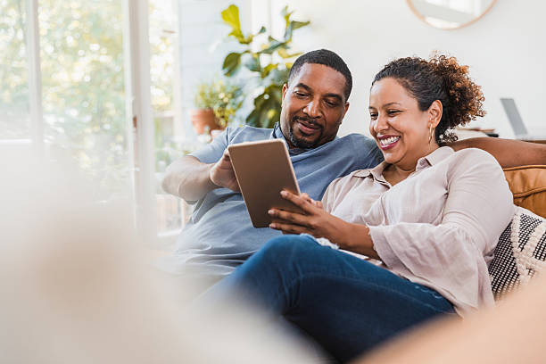 istock Smiling couple relaxing on a couch, looking at a digital tablet together. 2238143570