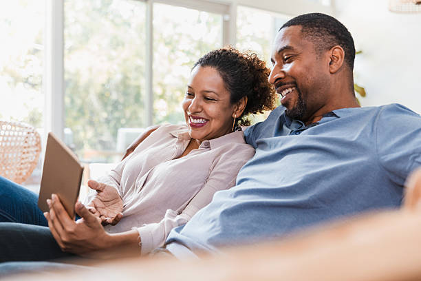 istock A Black couple relaxes on a sofa, watching a digital tablet and smiling. 2238143582