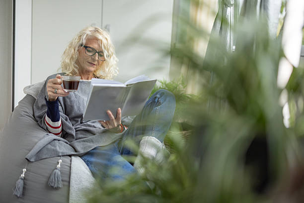 istock Senior Woman Reading a Magazine with Coffee While Relaxing on a Couch by Plants 2238162563