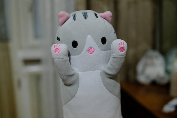 A gray stuffed kitten raises its paws, inside a house.