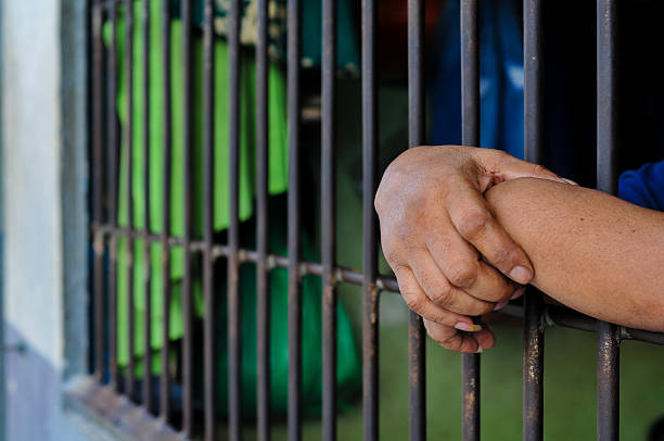 istock prisoner's hands behind bars with black background 2238172395