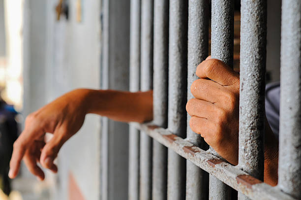 istock prisoner's hands behind bars with black background 2238172427