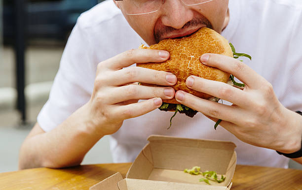 istock A young guy holds a burger in his hands while sitting in a cafe. 2238184788