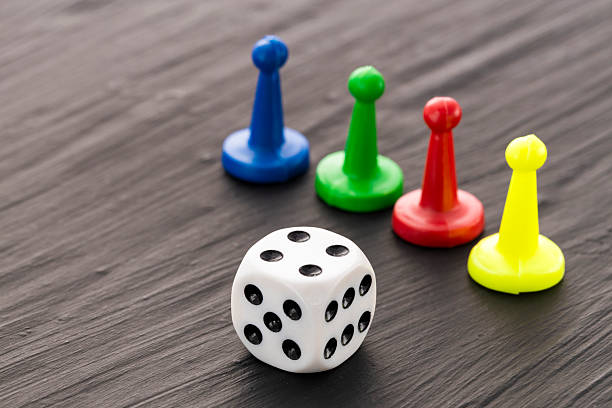 istock Colored game pieces and a white dice with black dots on a dark background 2238187353