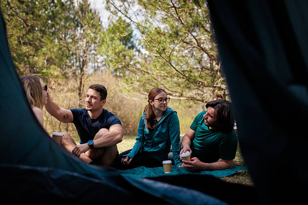 istock Friends enjoying a morning coffee while camping in a serene forest setting with sunlight filtering through the trees on a beautiful day 2238188210