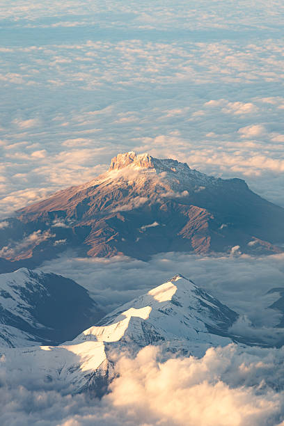 An awe-inspiring view from above the clouds, showcasing the dramatic peaks of the Greater Caucasus mountain range near Baku. The soft evening light casts a warm glow on the snow-dusted mountains, creating a serene and ethereal landscape. This image was taken at an altitude of 34,000 feet.