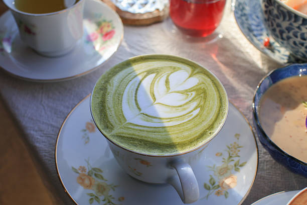 Hot Green Matcha Latte Art in luxury white cup on breakfast table setting. Healthy beverage in morning.