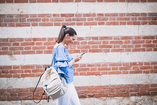 istock Young Woman Using Smartphone Walking by Brick Wall 2238194815