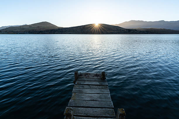 A wooden jetty leading out onto the still waters, surrounded by mountains in New Zealand’s South Island.