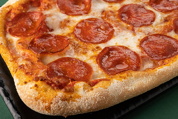 Delicious pepperoni pizza with golden crust, melted cheese, and savory toppings, presented on a black plate, showcasing appetizing textures and vibrant colors for culinary enjoyment