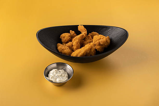 istock Crispy fried chicken pieces served in a stylish black bowl alongside a small silver dish of creamy dipping sauce on a vibrant yellow background 2238212563