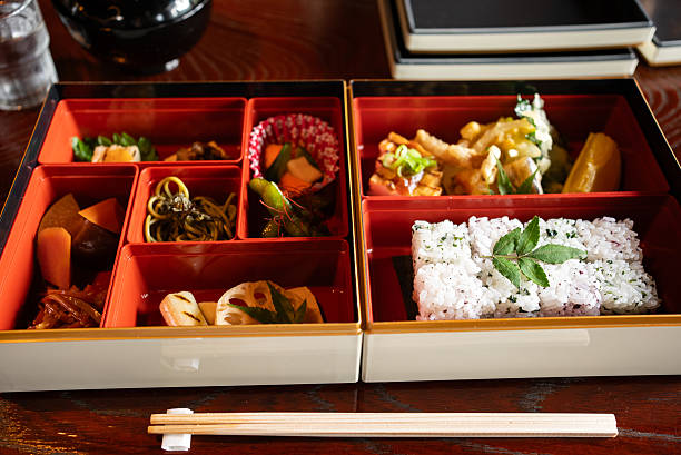 The jubako box contains vegetarian Japanese dishes: wakame seaweed and yukari-seasoned mixed rice, tempura, simmered dishes, and other accompaniments. Vegetarian cuisine.