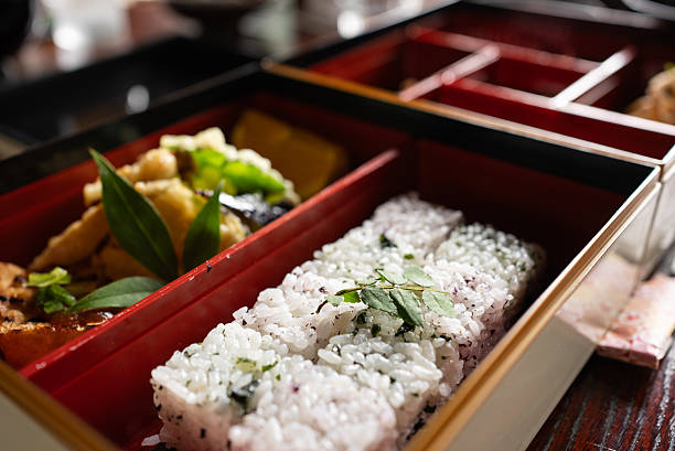The jubako box contains vegetarian Japanese dishes: wakame seaweed and yukari-seasoned mixed rice, tempura, simmered dishes, and other accompaniments. Vegetarian cuisine.