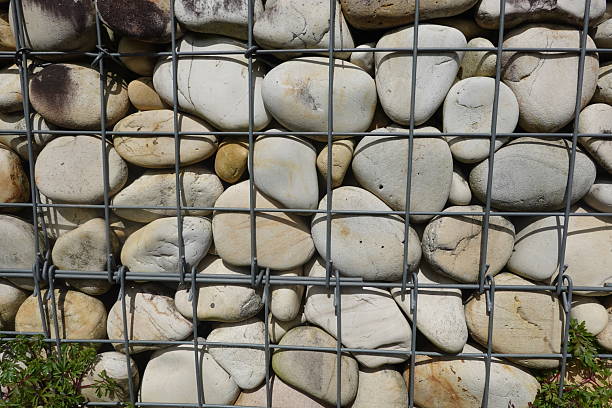 Metal mesh gabion retaining wall holding smooth, rounded river rocks, creating a textured and patterned background