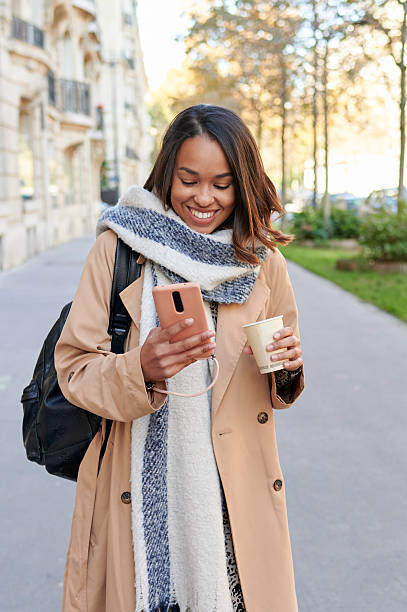 istock Woman using mobile phone and having coffee while walking on the street 2238221905
