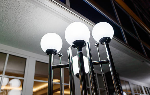 Four white lights are on a metal pole. The lights are on a building