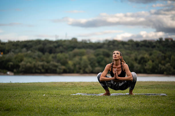 Yoga instructor practicing garland pose on yoga mat in nature near river, promoting health, wellness, and mindfulness