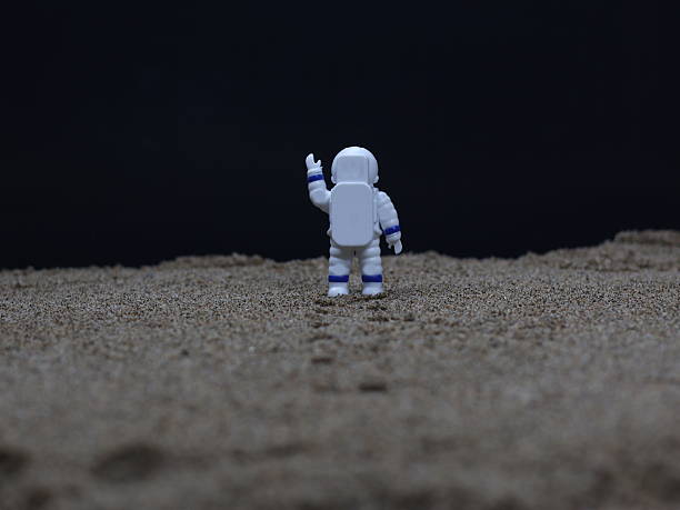A miniature astronaut stands on a surface resembling a planetary landscape, with footprints visible in front of him.