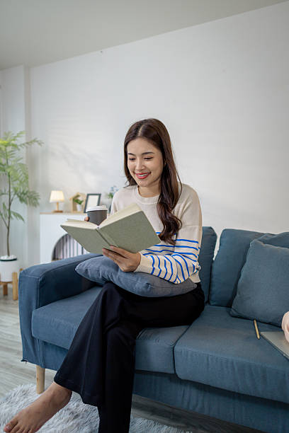 istock A young woman sits comfortably on a sofa, reading a notebook while holding a coffee cup. She looks relaxed and focused, enjoying a calm moment of study or planning at home. 2238239111