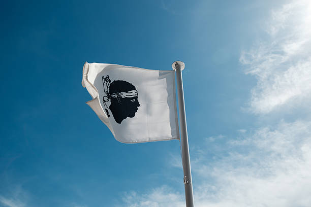 The Moors head of the Corsican flag fluttering in the wind on a flagpole against a deep blue sky