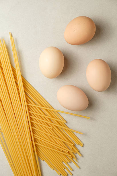 Bright scene showing four fresh eggs beside a bundle of uncooked spaghetti on a light countertop. Ingredients are ready for a delicious pasta dish, evoking a cozy kitchen atmosphere.