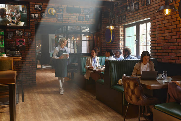 Happy waitress using touchpad while walking through a bar and talking to her customers.