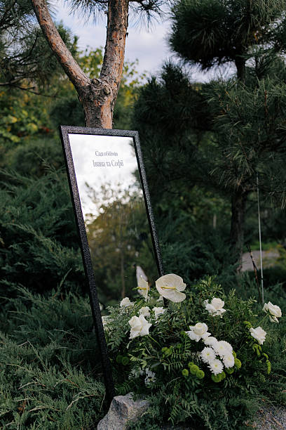 Elegant Wedding Welcome Sign Mirror Displayed Outdoors Amidst White Flowers and Pine Trees