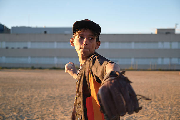 Young male baseball player throwing baseball on field, concentrating during a game or practice