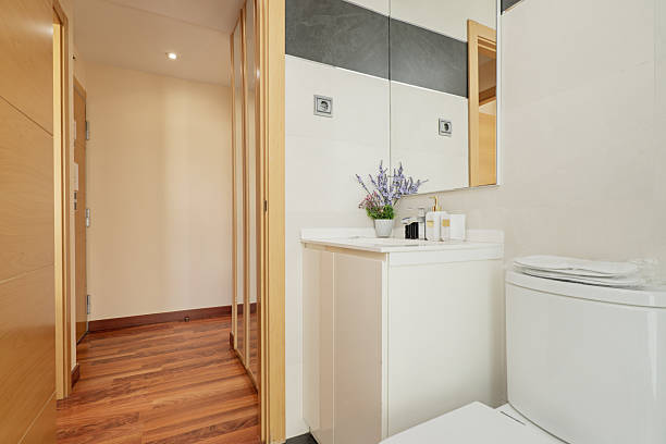 istock Small bathroom with a white porcelain sink above a white cabinet with doors, a wall mirror and reddish flooring 2238255984
