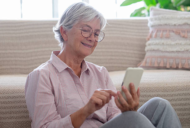 istock Happy senior woman sitting at home using smartphone for message text, social, connection. Elderly woman smiling and enjoying relax with technology, online communication, and digital lifestyle in a cozy living room. 2238256955