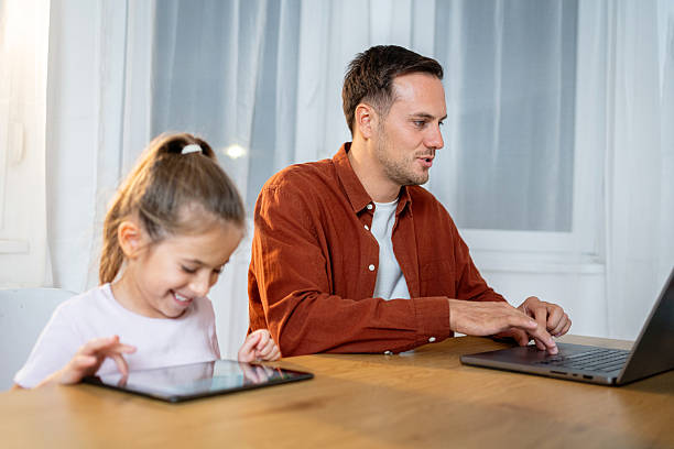 istock Father works from home on laptop while daughter uses tablet beside him 2238265892