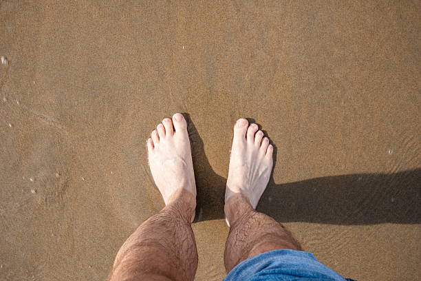istock Caucasian male bare feet and pulled up jeans, standing on a sandy beach. Top down, close up view 2238268416