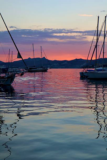 istock A tranquil harbor at sunset with colorful clouds and a vibrant red-orange sky reflecting on the calm water, framed by silhouettes of docked sailboats. 2238269259