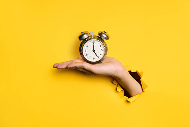 istock Vintage alarm clock in hand over yellow background 2238271544