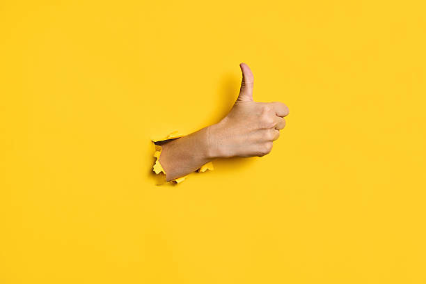 istock Thumb up hand gesture through hole in torn yellow paper background 2238271555