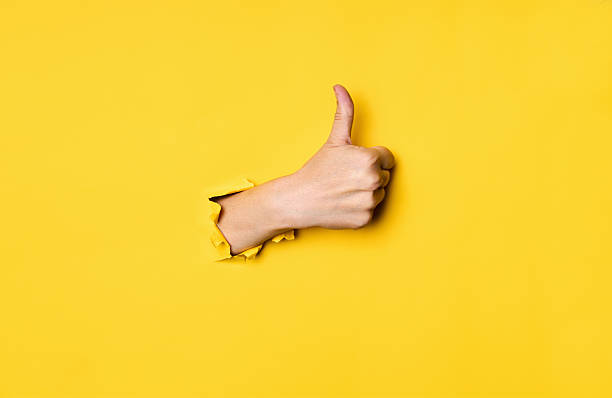 istock Thumb up hand gesture through hole in torn yellow paper background 2238271557