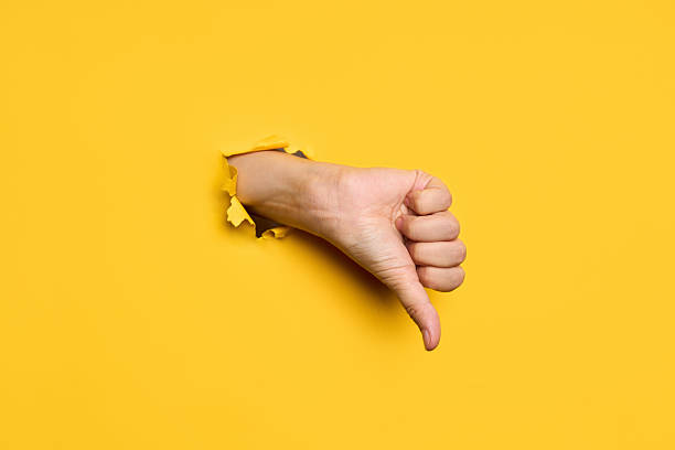 istock Thumb down sign gesture through hole in torn yellow paper background 2238271565