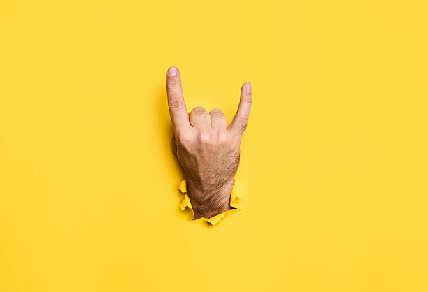istock Rock sign gesture through hole in torn yellow paper 2238271572