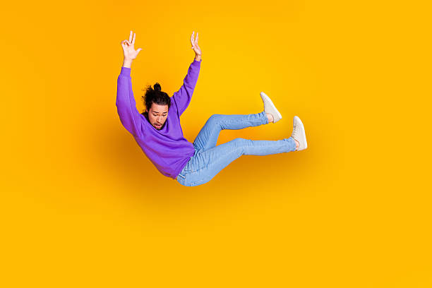 istock Young man in casual style falling against vibrant yellow backdrop showcasing movement and expression with playful purple hoodie 2238271689