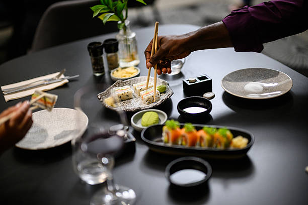 Hands with chopsticks reaching toward an assorted sushi platter with fashion sandwiches during a shared restaurant dinner
