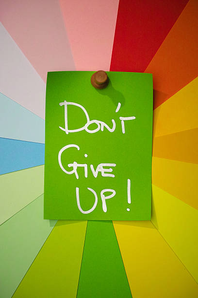 istock Green paper note pinned to a colorful array of different pastel rainbow colored note papers set in a circular spiral, with the inspirational words 'DON'T GIVE UP !' written on it. 2238274290